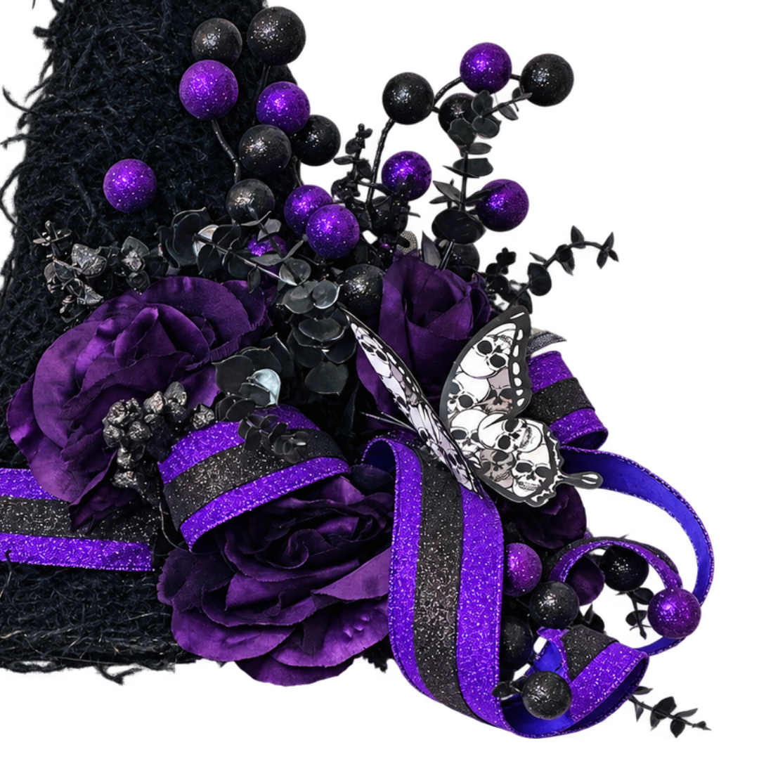 A decorative witch hat door hanger with a tall black brim, purple and black glitter ribbon, purple artificial roses, black and purple round glitter balls and butterfly embellishments on a plain white background by Monkey's Creations.