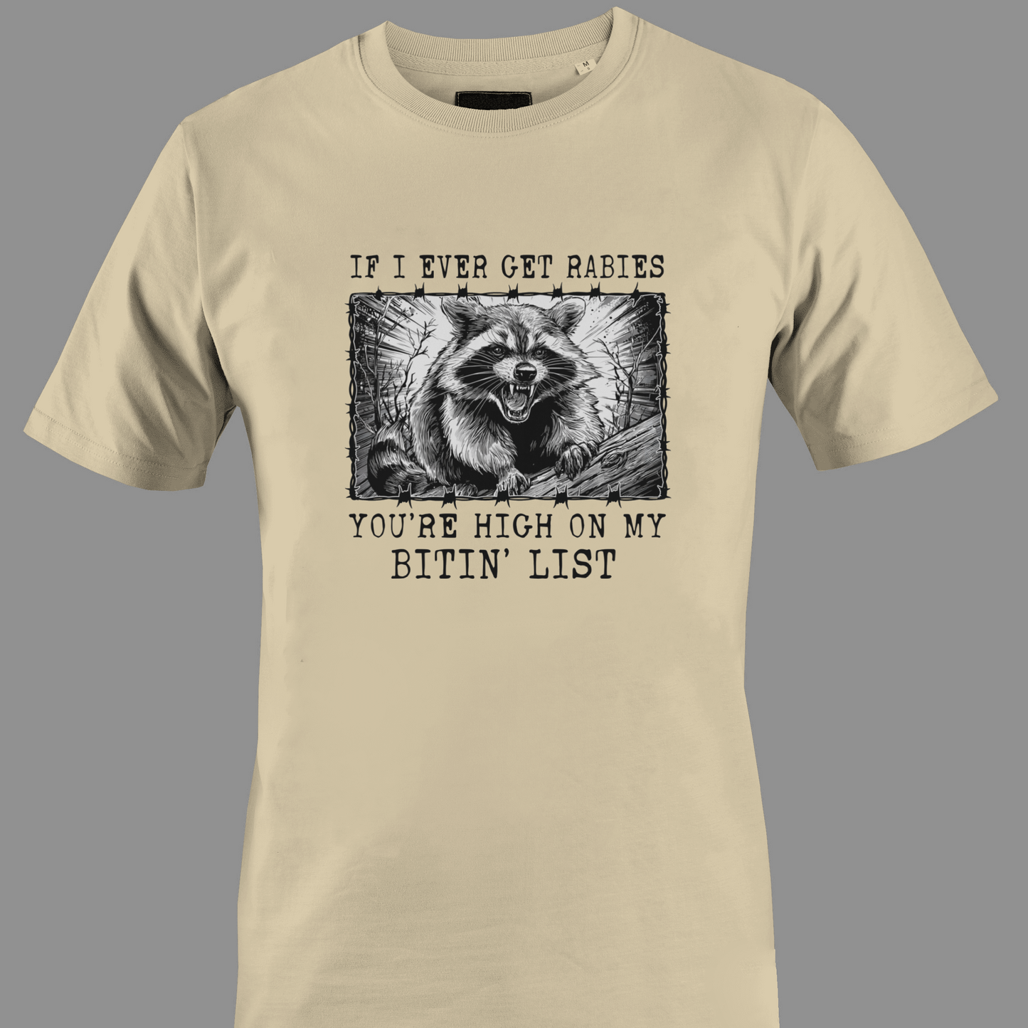 Beige t-shirt with a graphic of a raccoon and text rabies bite list 