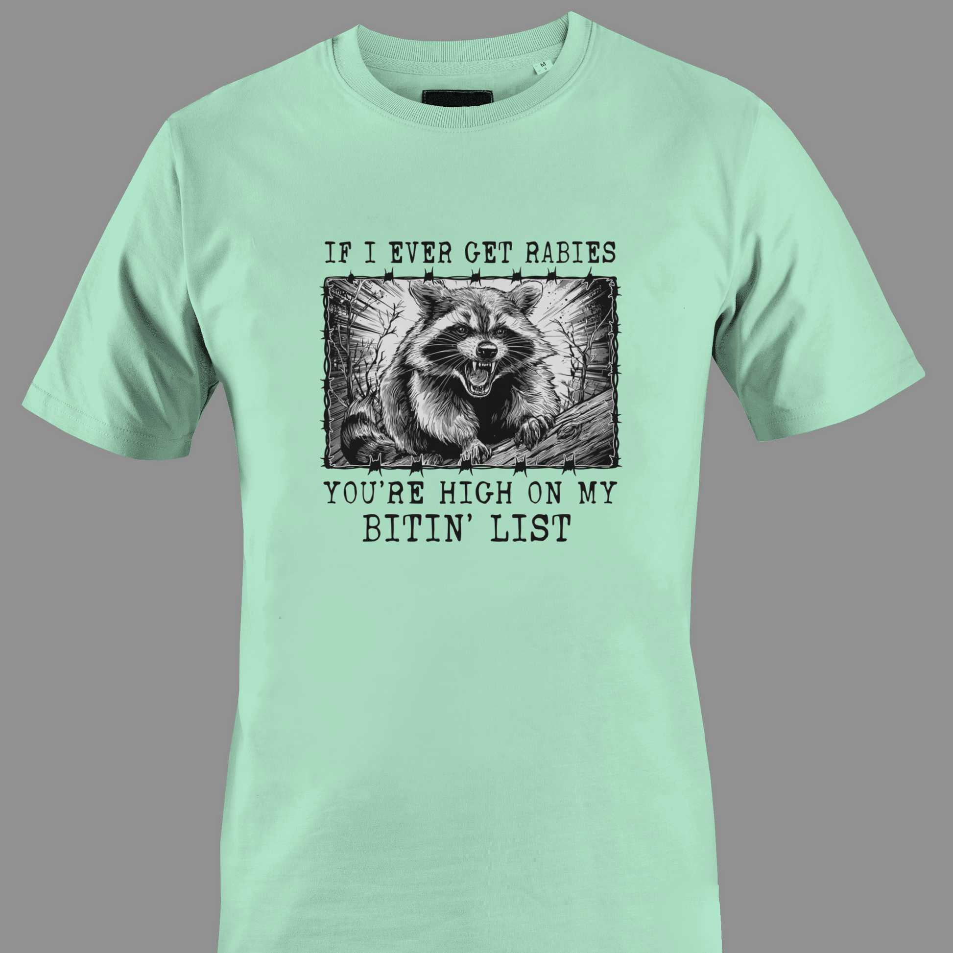 Light green t-shirt with a graphic of a raccoon and text rabies bite list 