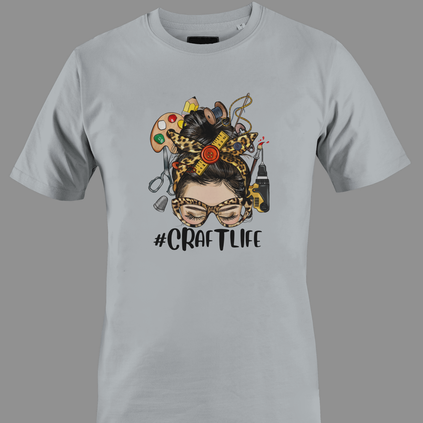 Light gray t-shirt with a graphic design featuring a woman's face with craft supplies around her head, featuring the hashtag #CRAFTLIFE.