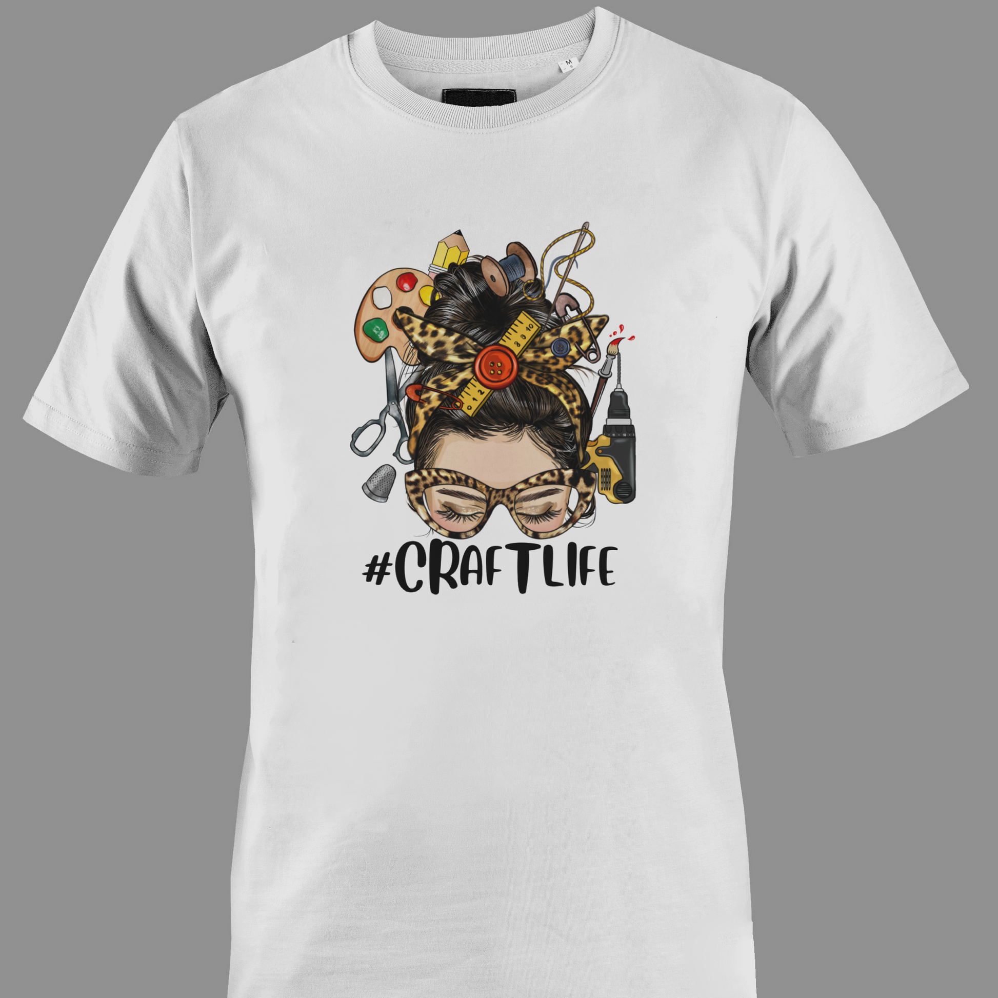 White t-shirt with a graphic design featuring a woman's face with craft supplies around her head, featuring the hashtag #CRAFTLIFE.
