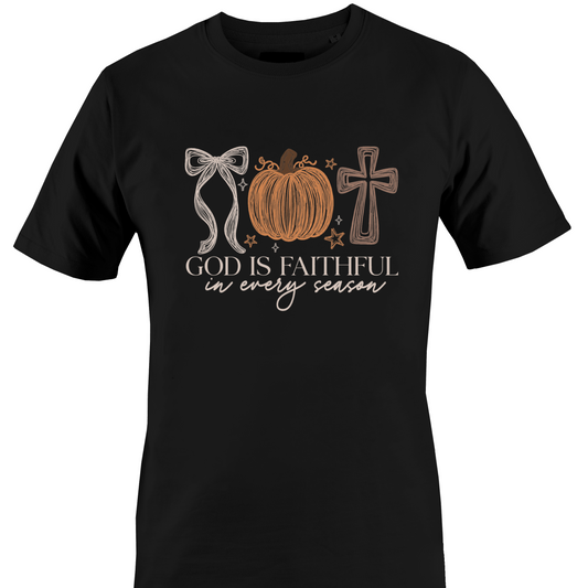 A black short-sleeve crewneck t-shirt featuring a graphic design on the front with a bow, a pumpkin, a cross, and the text 'GOD IS FAITHFUL in every season' by Monkey's Creations.