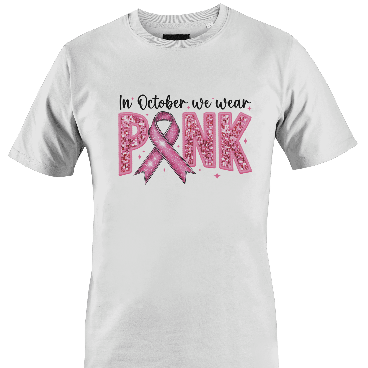 A white short-sleeve crewneck t-shirt featuring a pink graphic on the front that reads 'In October we wear PINK' with a pink ribbon and glitter-textured letters by Monkey's Creations. 