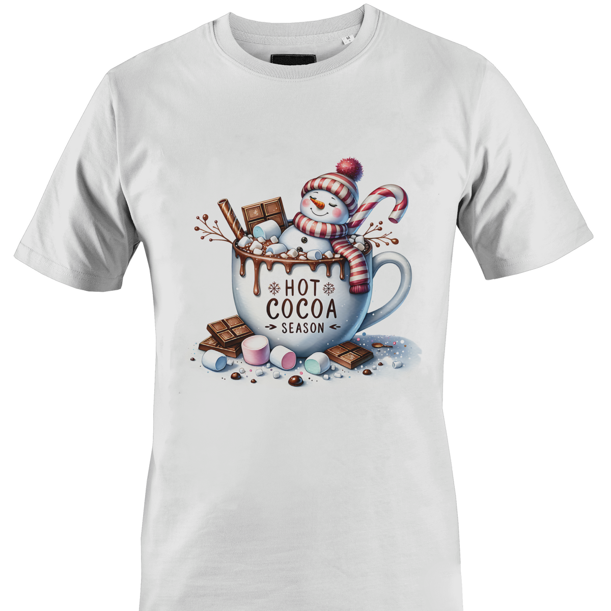 A white short-sleeve crewneck t-shirt featuring a colorful graphic print of a winter snowman wearing a red and white striped scarf, sitting in a white mug filled with hot cocoa, chocolate chunks, marshmallows, and a candy cane. The text 'HOT COCOA SEASON' is printed on the mug by Monkey's Creations.