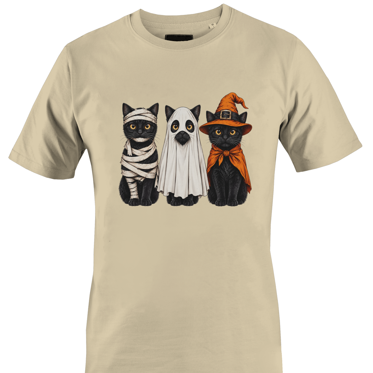 A beige short-sleeve crewneck t-shirt featuring a graphic print of three black cats dressed in Halloween costumes (as a mummy, a ghost, and as a witch) by Monkey's Creations.