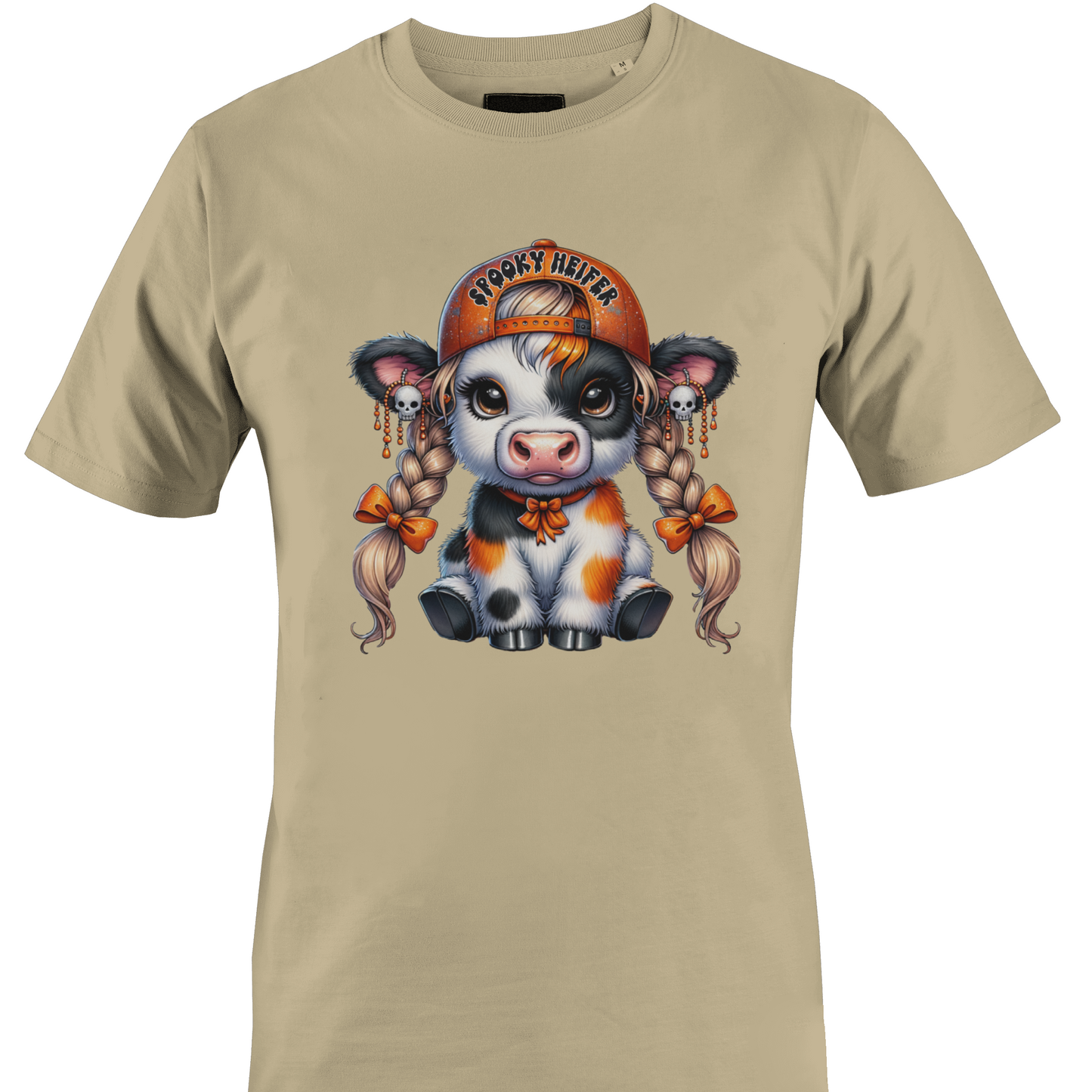 A tan short-sleeve crewneck t-shirt featuring a colorful graphic of a cute cartoon cow wearing an orange baseball cap with the text 'spooky heifer' by Monkey's Creations.
