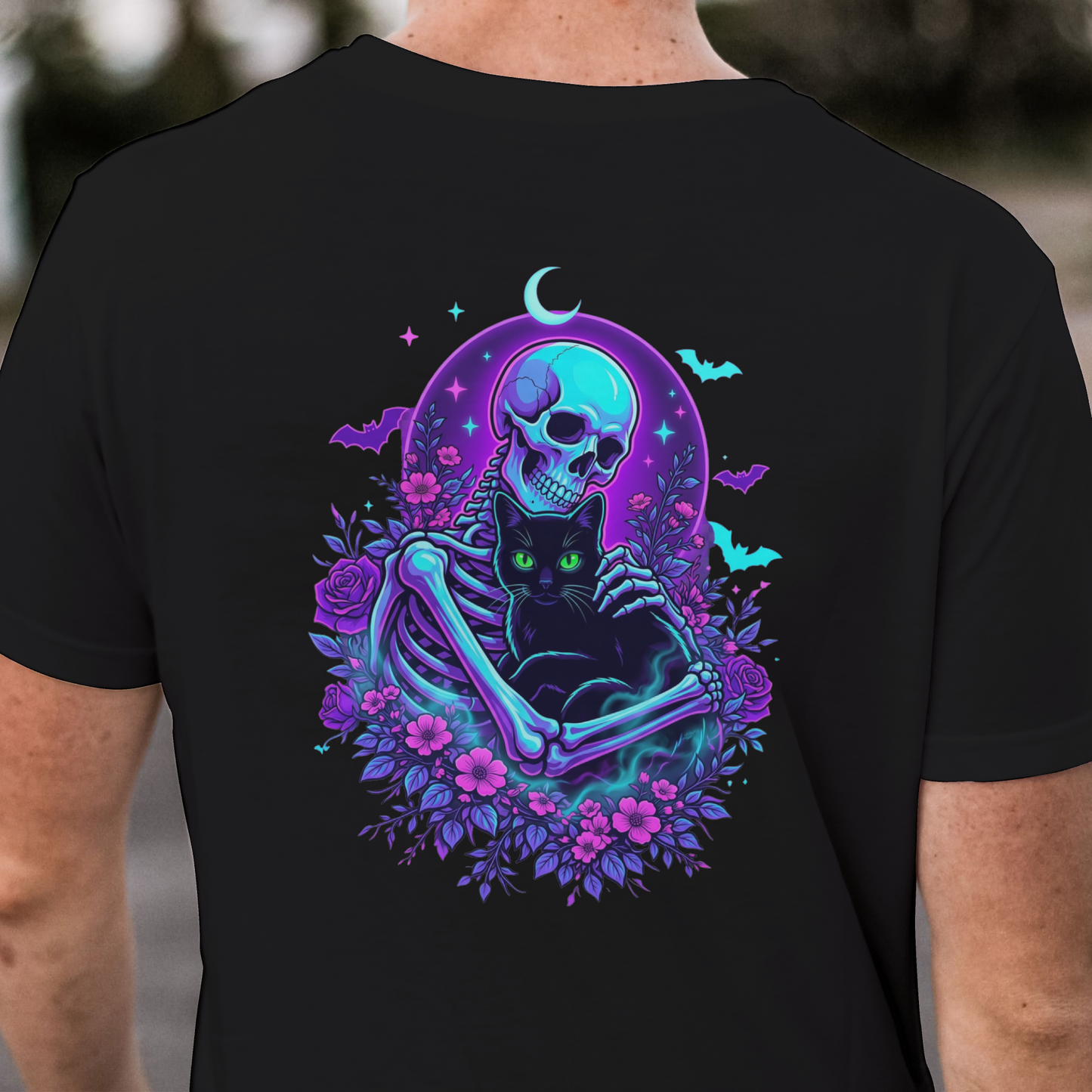 Black t-shirt with a swirl of dark purple, pink and teal bats front and a skeleton in front of a full moon holding a black cat surrounded by teal, pink and purple flowers and bats on the back by Monkey's Creations.