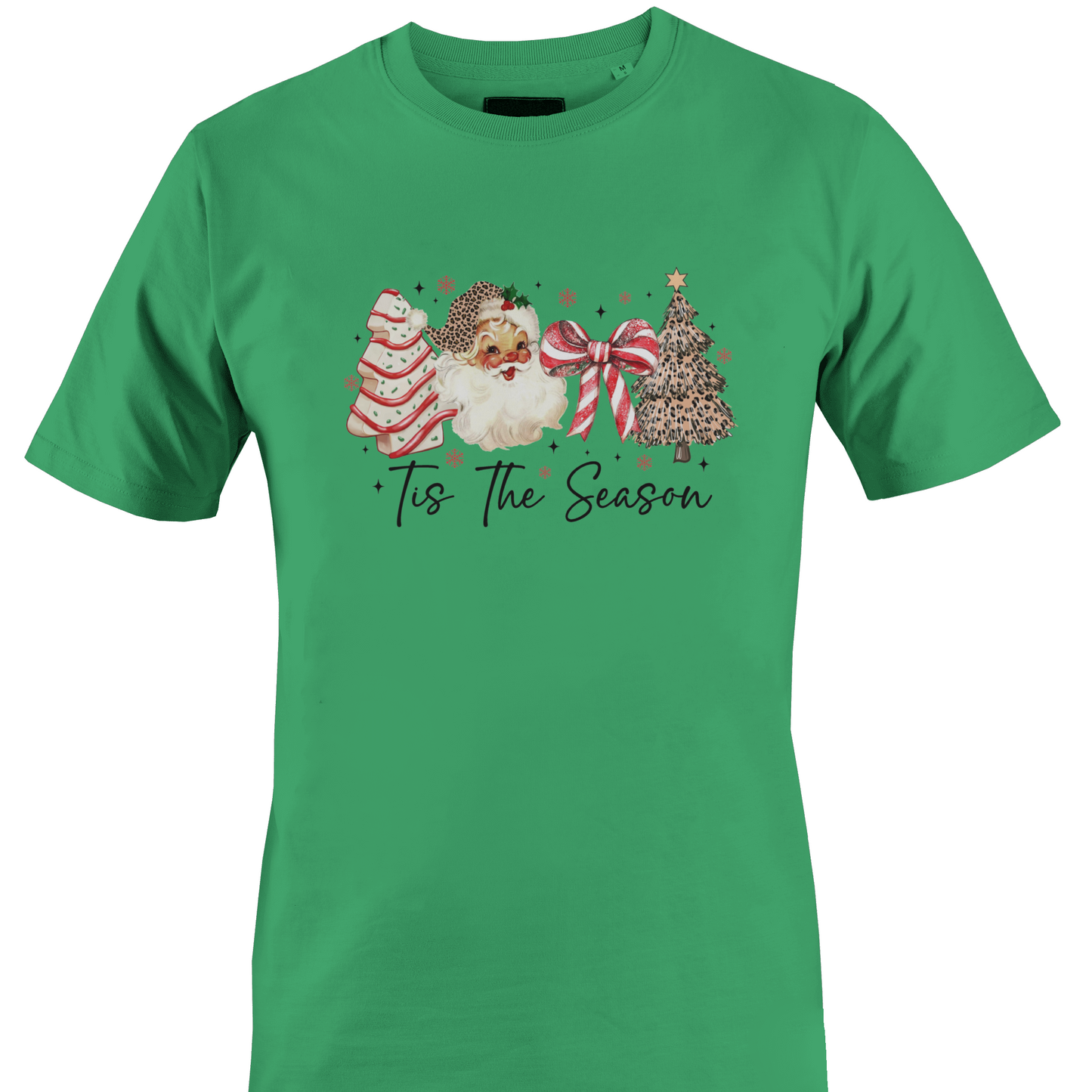 A green short-sleeve crewneck t-shirt featuring a festive Christmas graphic on the chest. The graphic depicts a watercolor Santa Claus, a decorated Christmas tree, a striped ornament, and a large red bow, with the text 'Tis The Season' written below in a black script font by Monkey's Creations.