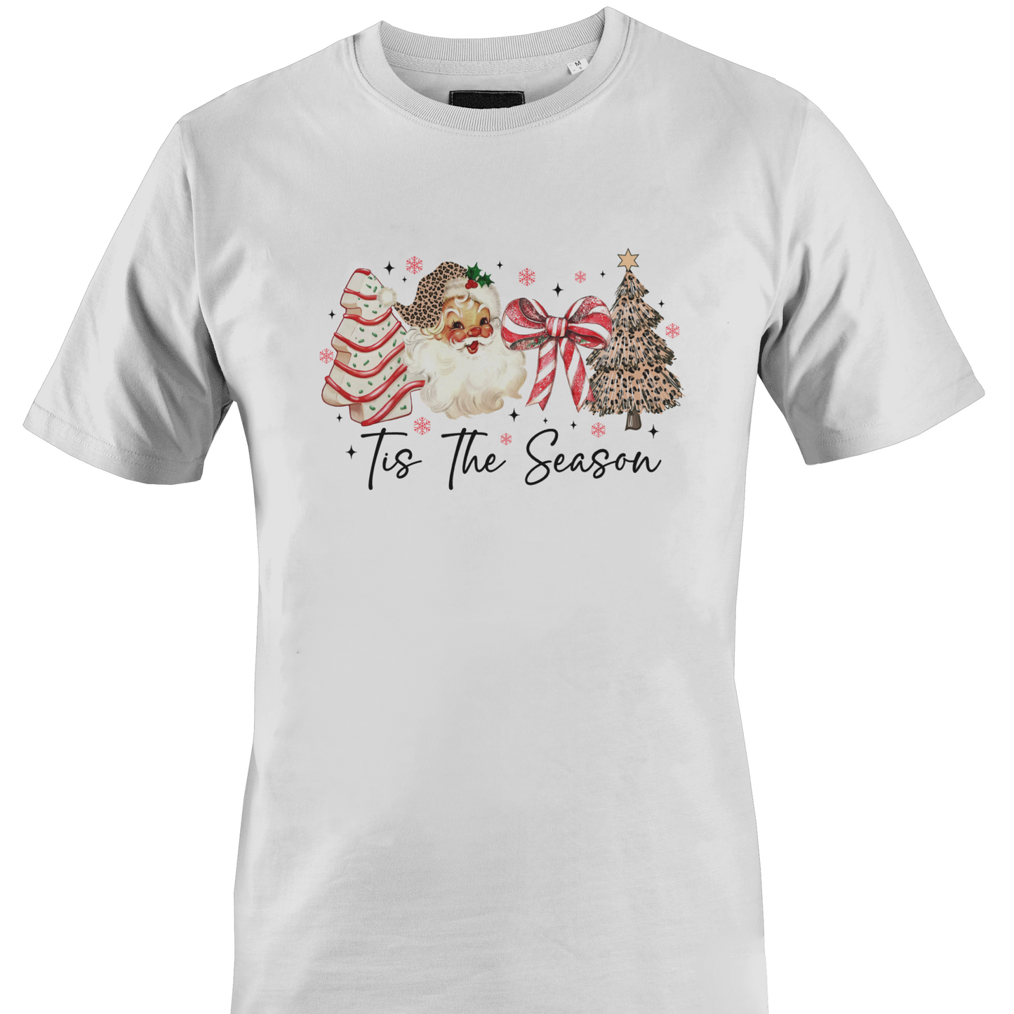 A white short-sleeve crewneck t-shirt featuring a festive Christmas graphic on the chest. The graphic depicts a watercolor Santa Claus, a decorated Christmas tree, a striped ornament, and a large red bow, with the text 'Tis The Season' written below in a black script font by Monkey's Creations.