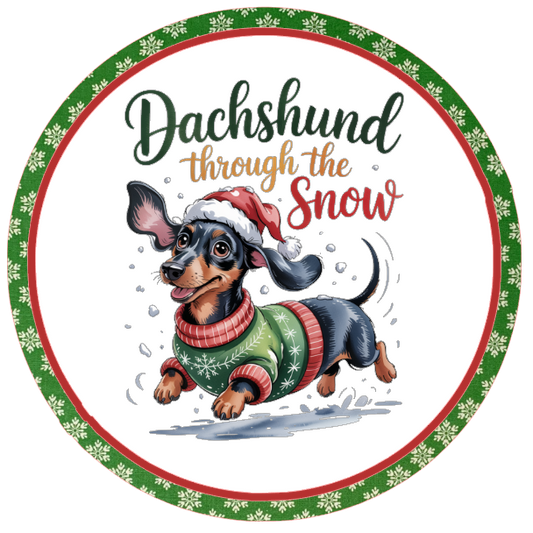 Round wreath sign with a dachshund wearing a sweater and Santa hat, text 'Dachshund through the snow', on a white background.