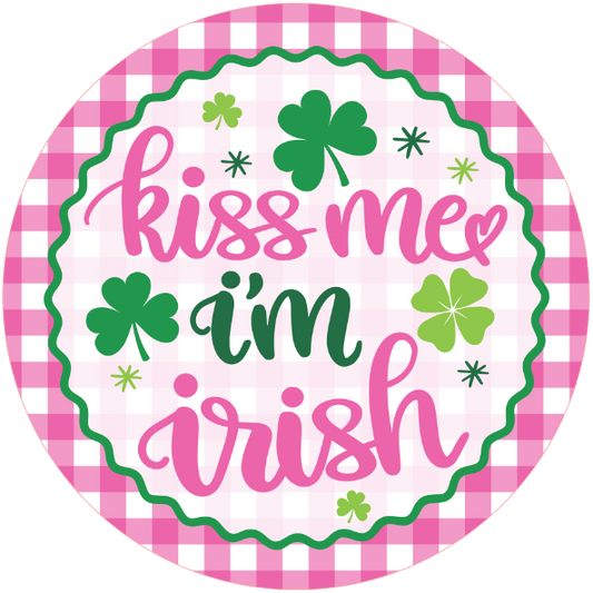 Round metal wreath sign with 'kiss me I'm Irish' text and shamrock symbols on a pink checkered border.
