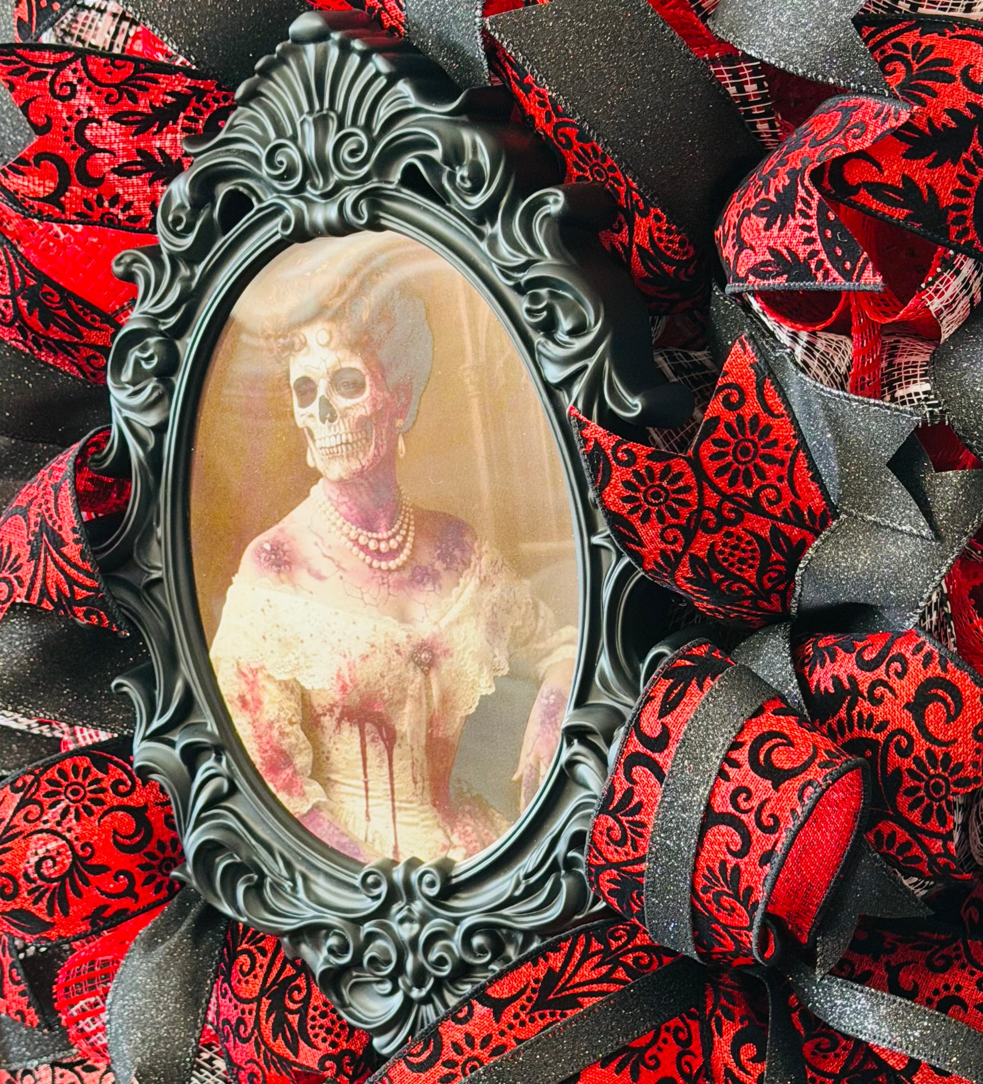 Round red and black vintage damask inspired deco mesh and ribbon wreath with with a photo of a lady / skeleton in the middle that changes to a creepy skeleton when the viewing angle is changed by Monkey's Creations.