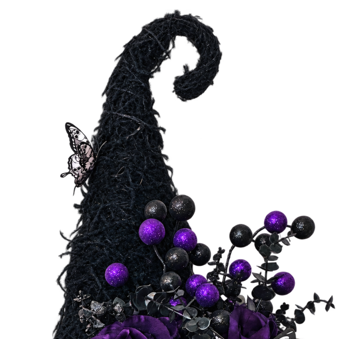 A decorative witch hat door hanger with a tall black brim, purple and black glitter ribbon, purple artificial roses, black and purple round glitter balls and butterfly embellishments on a plain white background by Monkey's Creations. 