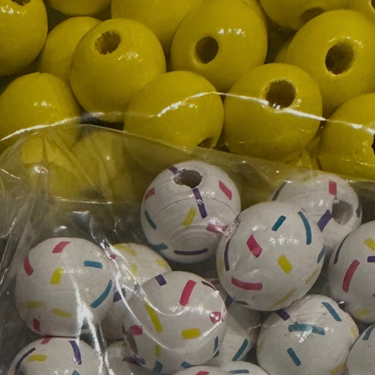 close up of yellow wooden beads and white beads with colorful confetti 
